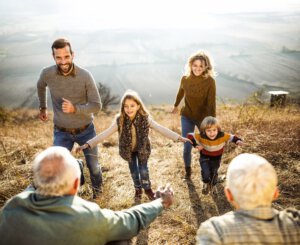 Junge glückliche Familie, die den Hügel hinauf in die Umarmung ihrer Eltern und Großeltern rennt.